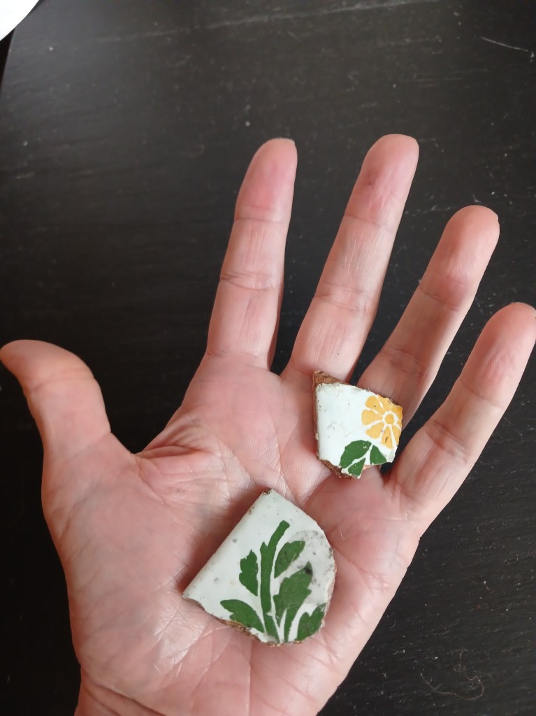A white hand holding two pieces of broken pottery with floral designs, resting on a dark surface.