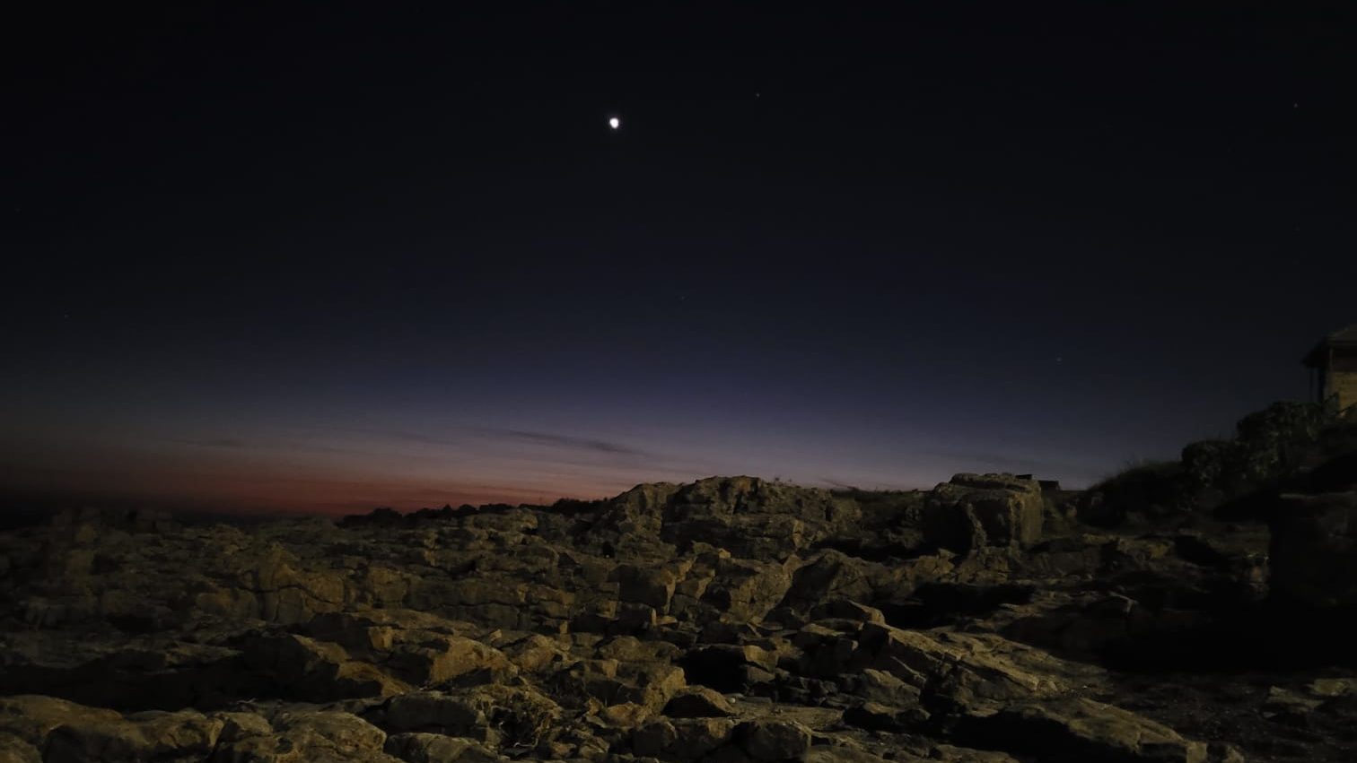 Night scene featuring rocky terrain under a starry sky with a visible moon.