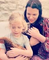 A young girl holding a chicken with a woman sitting beside her, both smiling