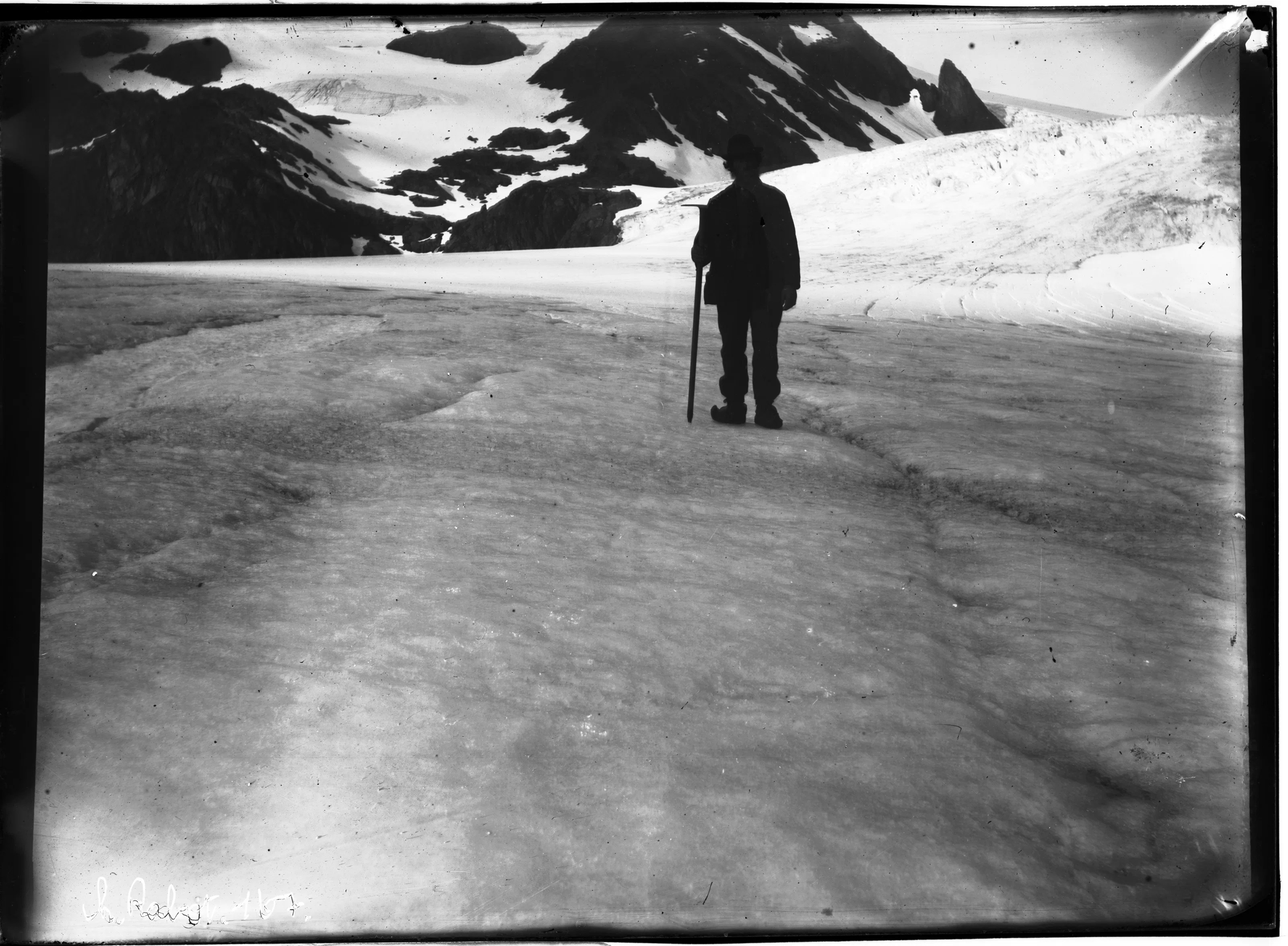 Silhouette of a person with a walking stick standing on a snowy glacier with mountains in the background
