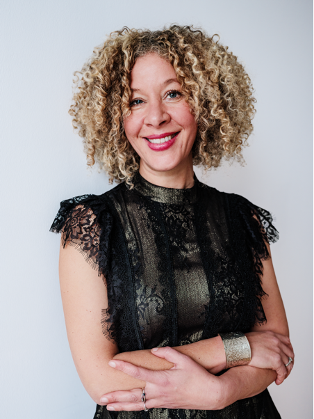 image A smiling woman with curly hair wearing a stylish black lace top against a plain white background